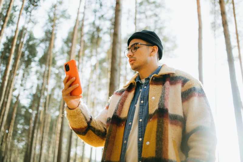 Człowiek z telefonem w lesie. Zdjęcie: Maksim Goncharenok / pexels.com.