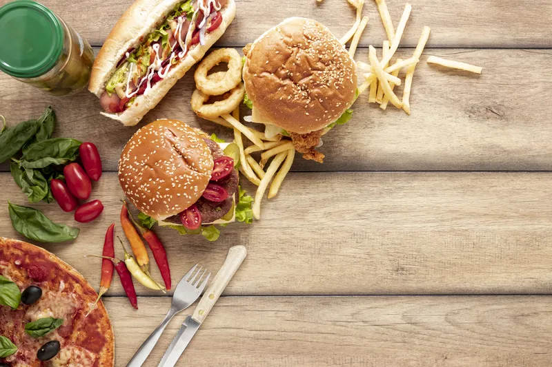 Drewniany stół z wyłożonym jedzeniem: fast foodami - hot dog, burgery, frytki, pizza